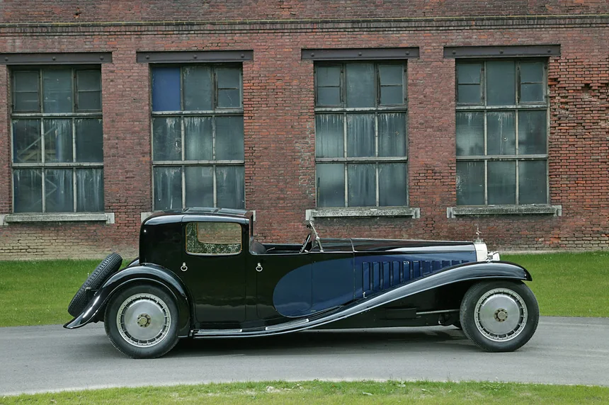 Black and blue classic Bugatti automobile beside a brick building